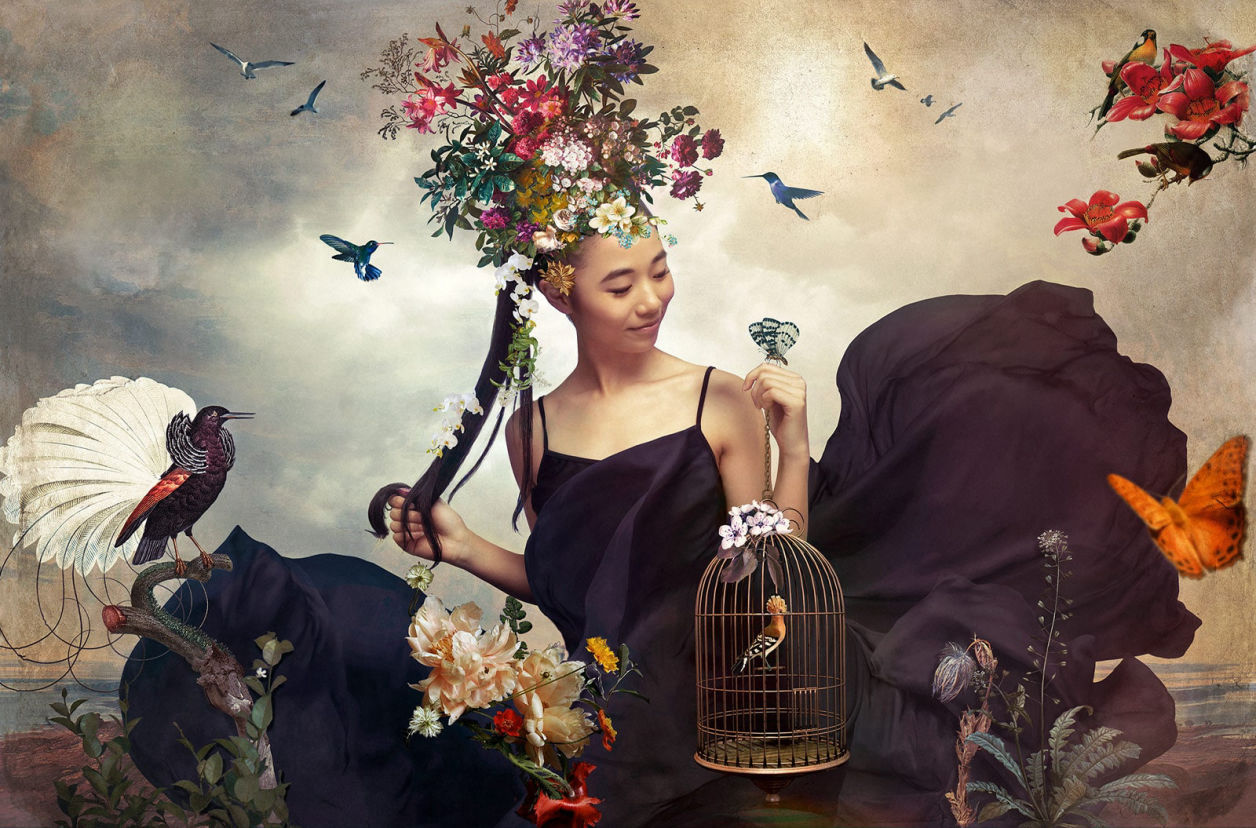 Painterly photography of a caucasian model wearing a gold dress surrounded by flowers and hummingbirds 